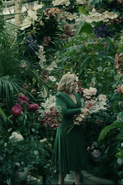Elena's vibrant green, surrounded by fading orchids. Costume as a fragile performance.
